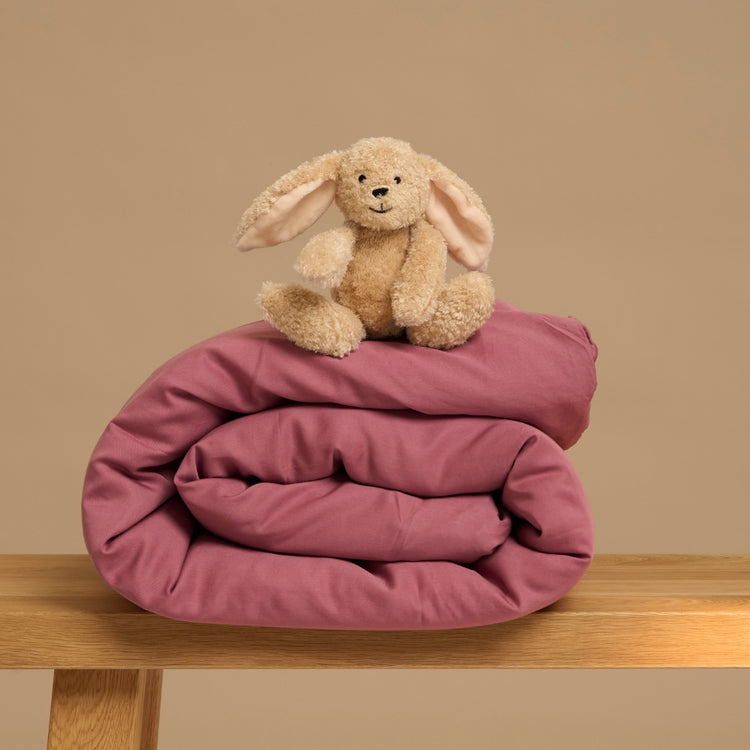 Op een krukje ligt een Tencel kinderdekbed van Coco & Cici met daarop een konijn. Het dekbedovertrek is in de kleur Dusty Rose, een donker roze.