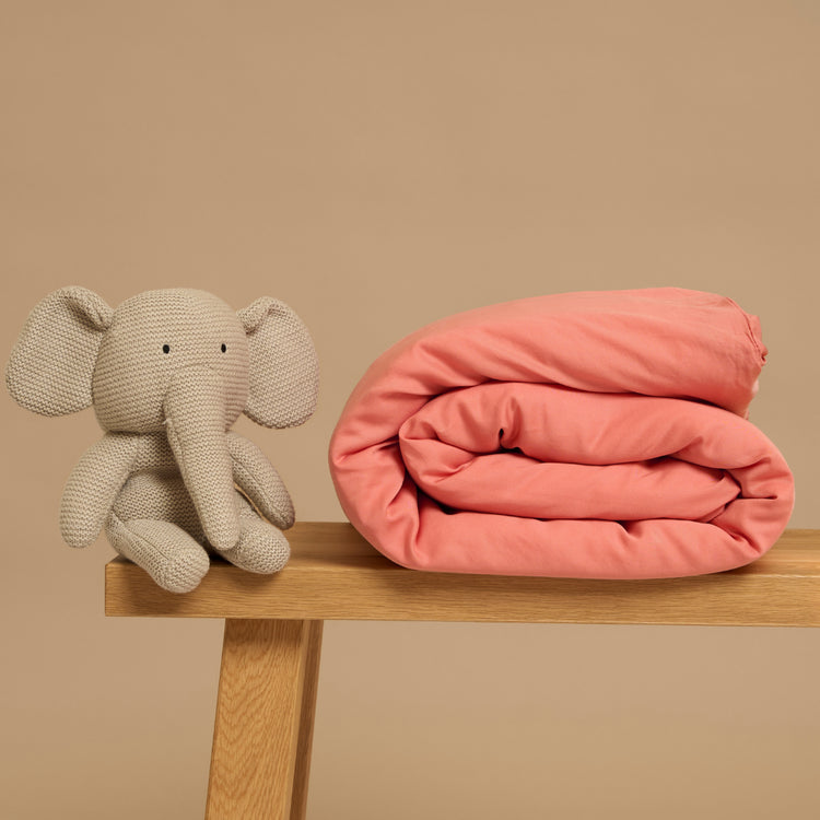 Een Tencel kinderdekbed van Coco & Cici in de kleur Blush, een tint roze, op een bankje met een olifantje ernaast.